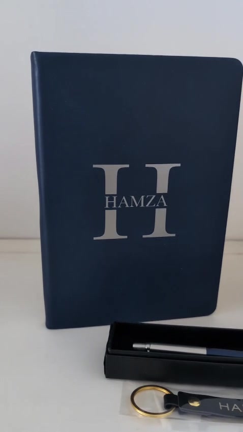 Navy notebook and flask with an H monogram, beside a boxed pen and a keychain
