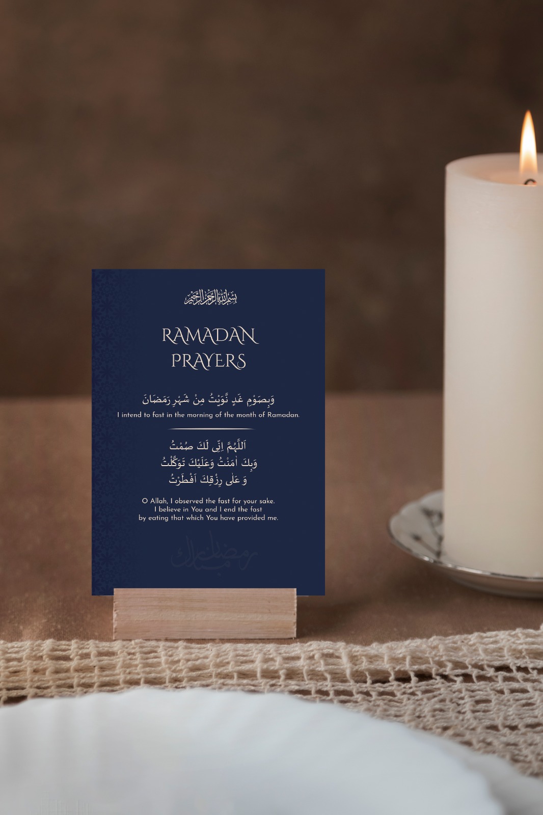A navy Ramadan dua card standing beside a lit candle
